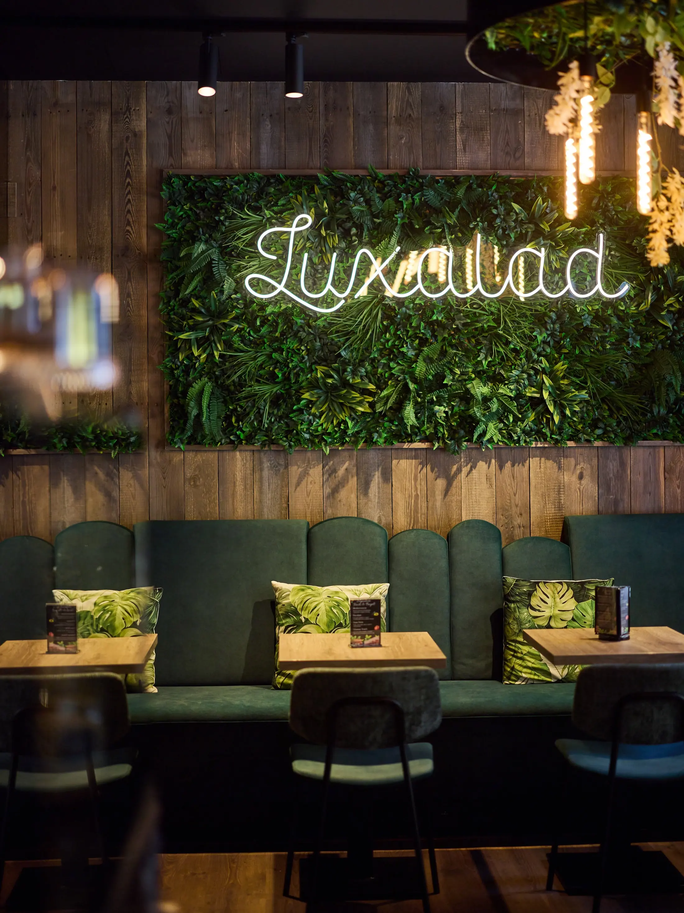 A Luxalad dining room — dark timber, green banquettes and a lit plant wall