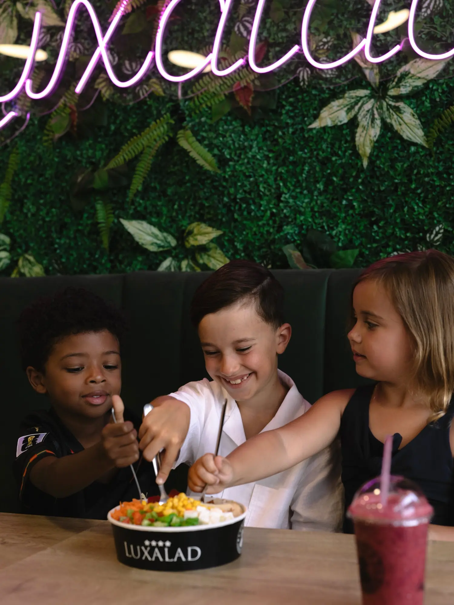 Children sharing bowls under the Luxalad neon