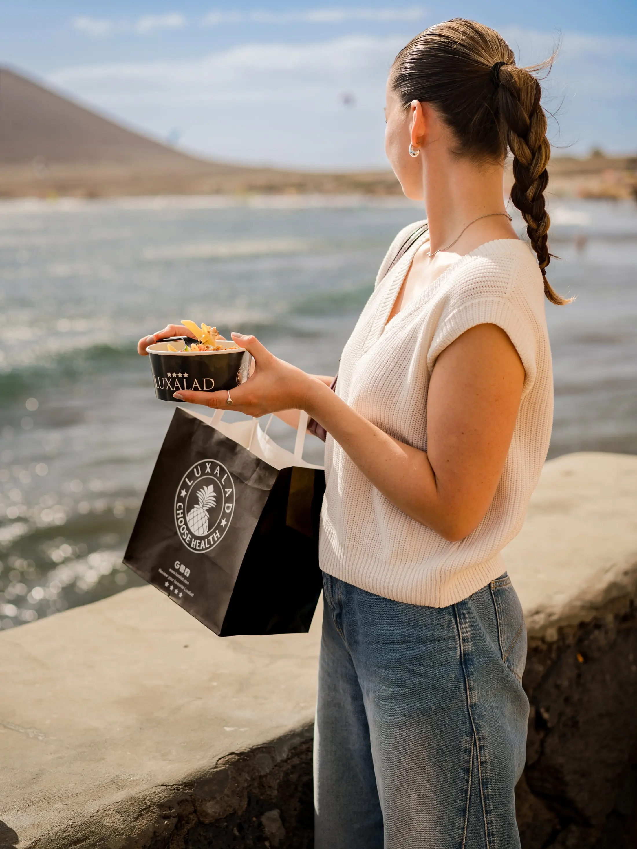 A guest holding a Luxalad bowl above the sea